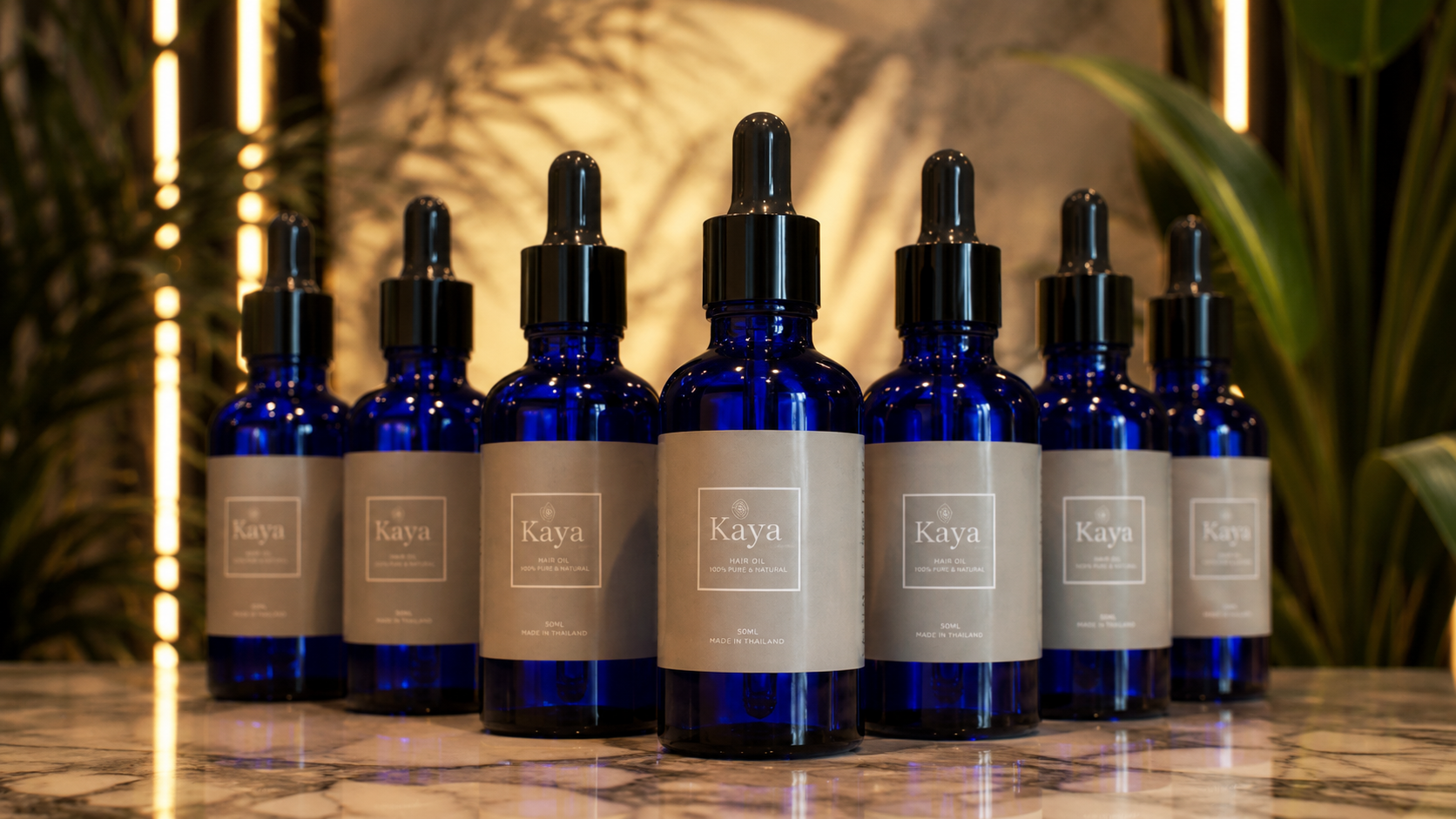 Kaya hair oil bottles displayed together on a marble surface with warm botanical lighting